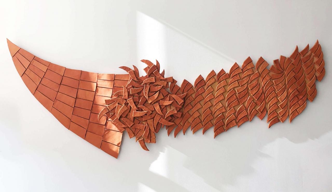 Ruskeista savitiilistä koostuva, veneen muotoinen taideteos, joka suoraviivaisempi ja ehjempi vasemmalla. Keskellä savitiilet muodostavat kaaoksen, joka rauhoittuu jälleen kohti oikeaa.