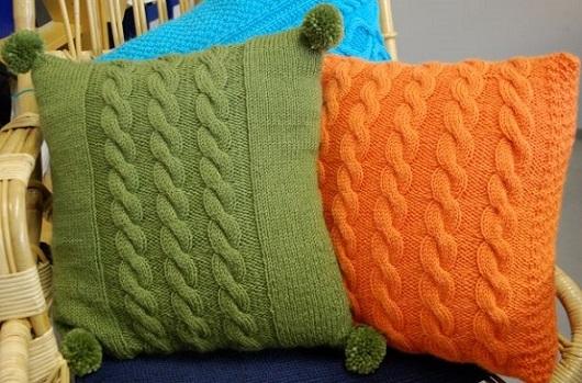 Kuvassa vihreä ja oranssi neulottu palmikkotyynynpäällinen aseteltuna korituoliin