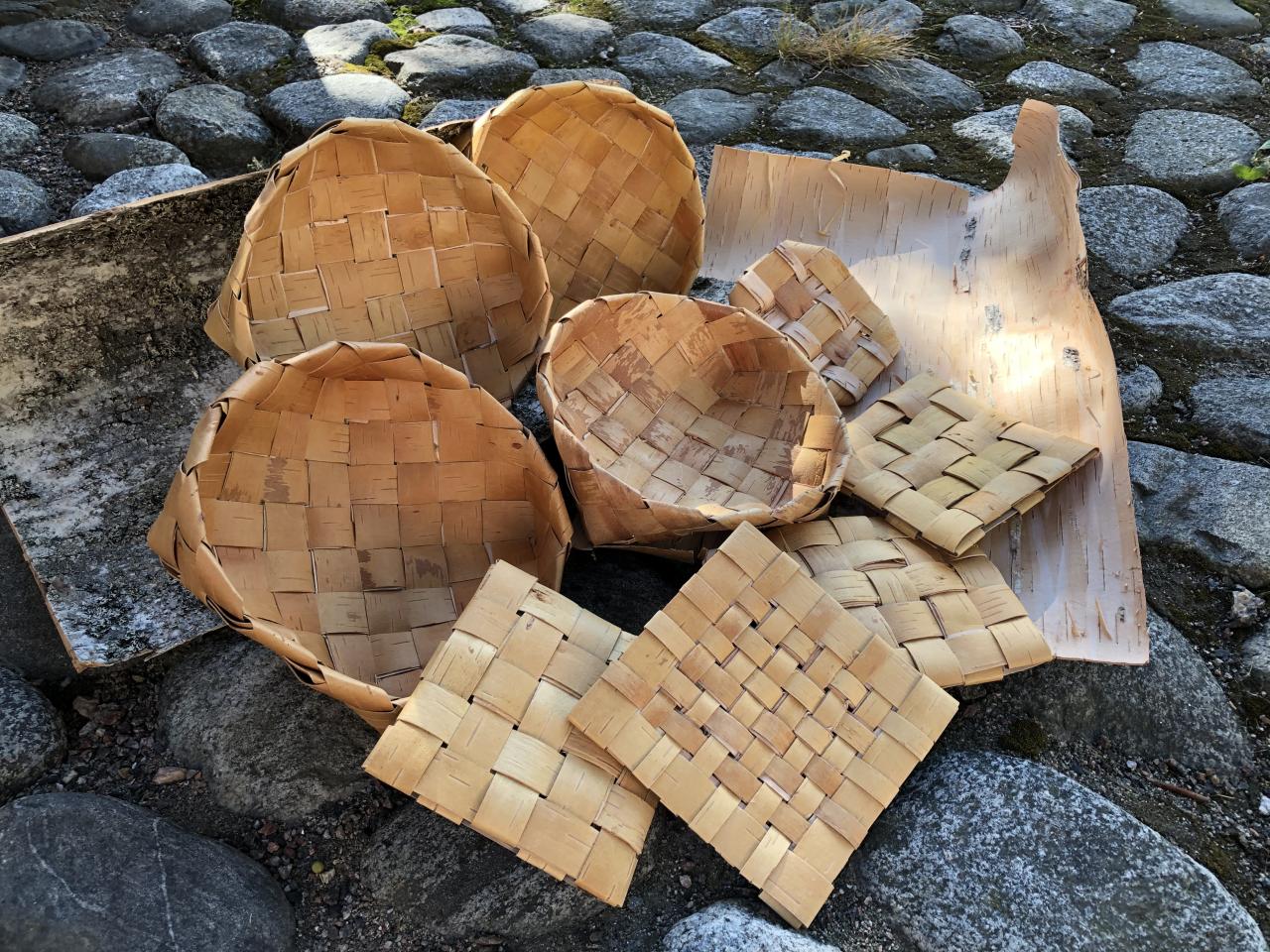 Vinopunonnalla valmistettuja tuohikoppia sekä suorapunonnalla valmistettuja tuohipannunalusia, taustalla pihakivetystä.