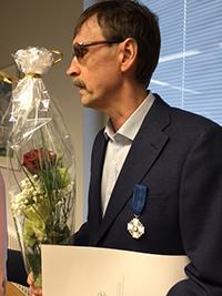 Teuvo Heikkosen puvun vasempaan rintapieleen on kiinnitetty Suomen valkoisen ruusun ritarimerkki ja hänellä on kädessään kukkakimppu.