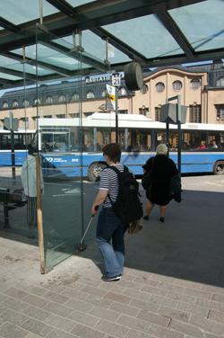 Nainen kävelee kohti bussipysäkillä olevaa lasiseinää.