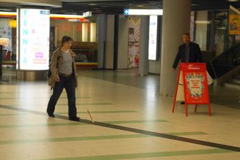 Nainen seuraa tummanväristä ohjaavaa raitaa Helsingin yliopiston metroasemalla.