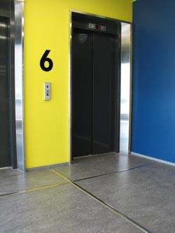 Ohjaava metallilista lattiassa hissin oven edustalla.