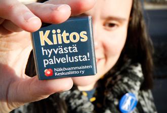 Kuva nuoresta naisesta pitämässä suklaaneliötä kädessään. Kääreessä lukee "Kiitos hyvästä palvelusta! Näkövammaisten Keskusliitto ry"