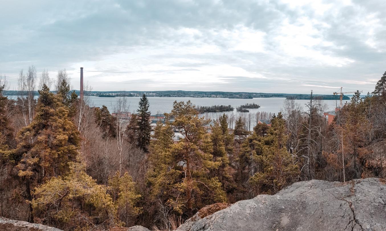 Maisema Pyynikinharjulta kohti Pyhäjärven maisemaa. Kuvassa näkyy mm. korkea piippu, saaria ja kaukana taustalla Pirkkala. Sää on pilvinen.