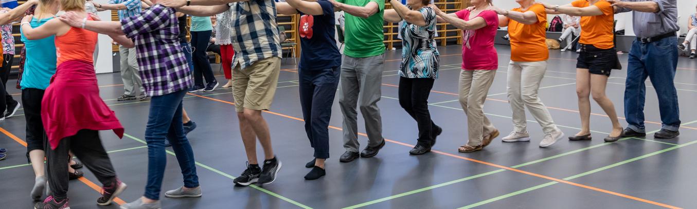 Kuvassa toistakymmentä jäsentä liikuntasalissa jonossa kädet edessä olevan olkapäillä