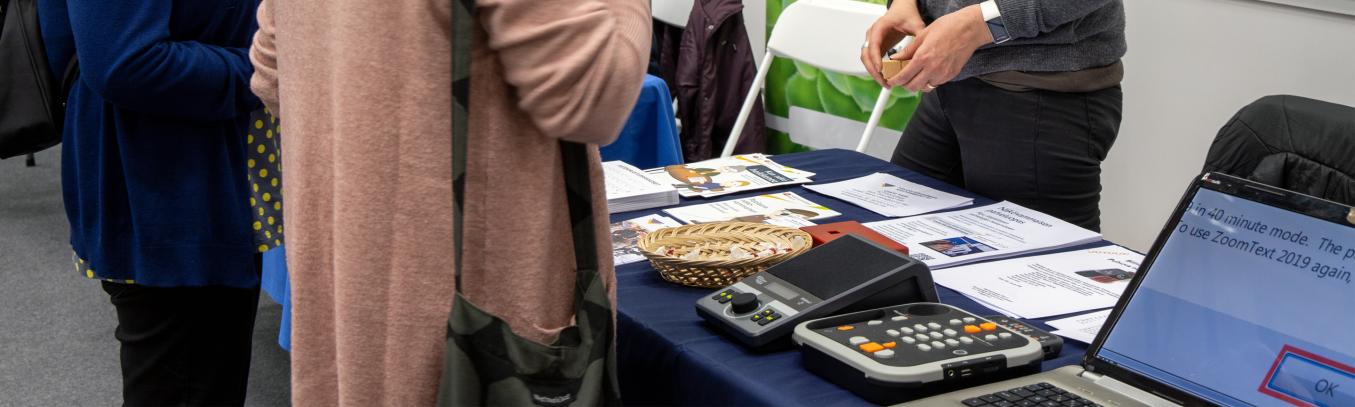 esittelypöytä, jossa on tietokone, daisysoittimia ja esitteitä