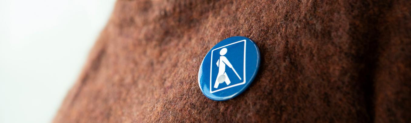 Näkövammaismerkki ruskeassa neulepuserossa.