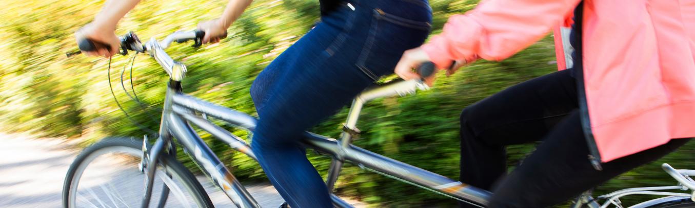 Kaksi henkilöä ajaa tandempyörällä. Kuvattu keskivartalosta alaspäin.